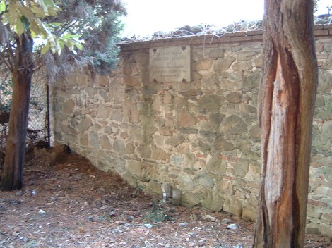 Lapide commemorativa posta su un muro di pietra, circondata da alberi e vegetazione.