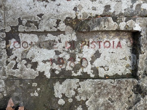 Cippo commemorativo con iscrizione in pietra, ricoperto di muschio e cenere, situato nella regione di Pistoia.