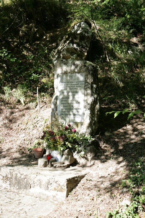 Cippo di Mòdine, una stele commemorativa circondata da fiori e candele, immersa nella natura.