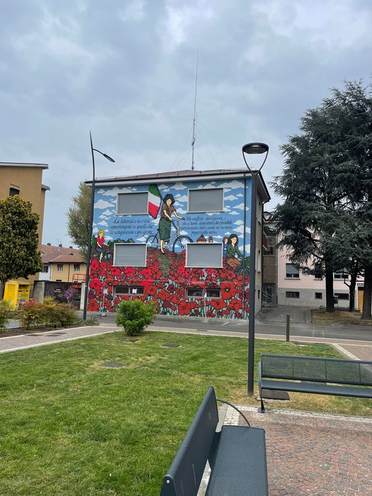 Murale commemorativo che omaggia le staffette partigiane, decorato con fiori rossi e simboli nazionali.