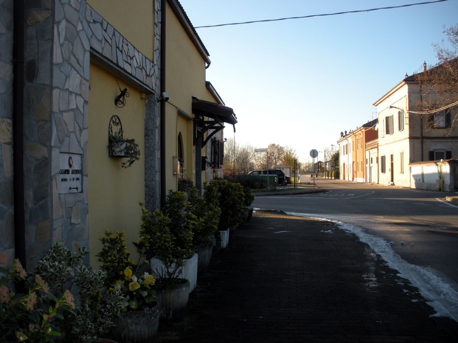 Vista di una strada con edificio e lapide dedicata a Casarini, circondata da piante e un'atmosfera serena.