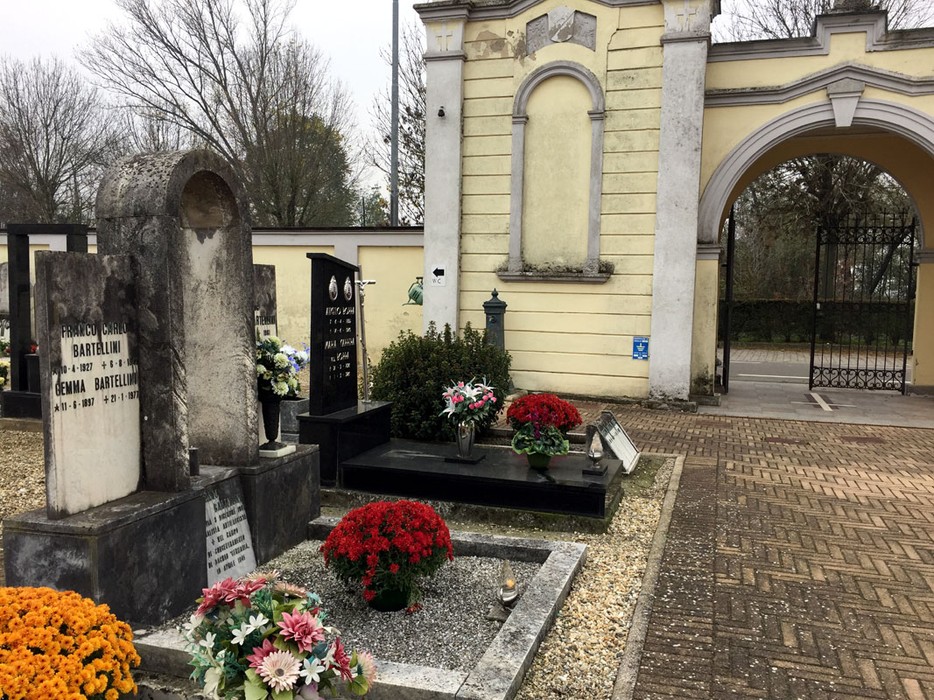 Sepolcro di Bartellini, con lapidi e fiori, in un cimitero tranquillo e curato.