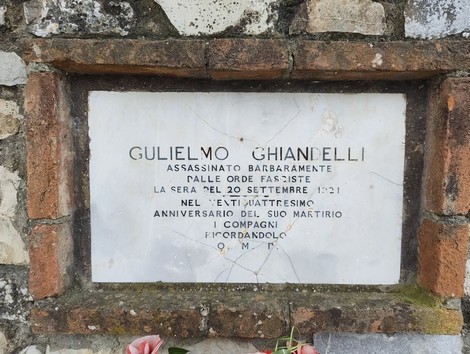 Lapide dedicata a Ghiandelli, commemorativa dell'assassinio avvenuto nel 1921, con fiori ai piedi.