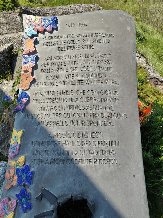 Lastra commemorativa in onore degli sminatori, decorata con fiori colorati e incisa con un messaggio significativo.