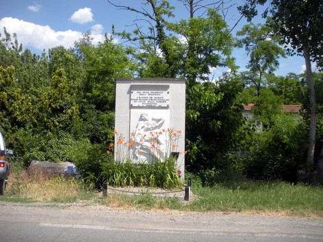 Monumento dedicato a Magnani e Cavallari, circondato da vegetazione e fiori, situato in un'area rurale.