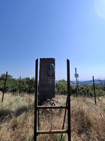 Stele di Ca' di Guzzo, monumento circondato da erba alta e paesaggio collinare sotto un cielo blue.