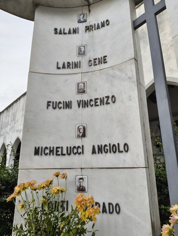 Sacrario dei deportati, commemorazione con nomi su marmo e fiori colorati in primo piano.