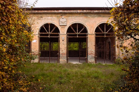Fronte del Poligono di tiro di Gonzaga, con archi e dettagli architettonici immersi nella vegetazione.
