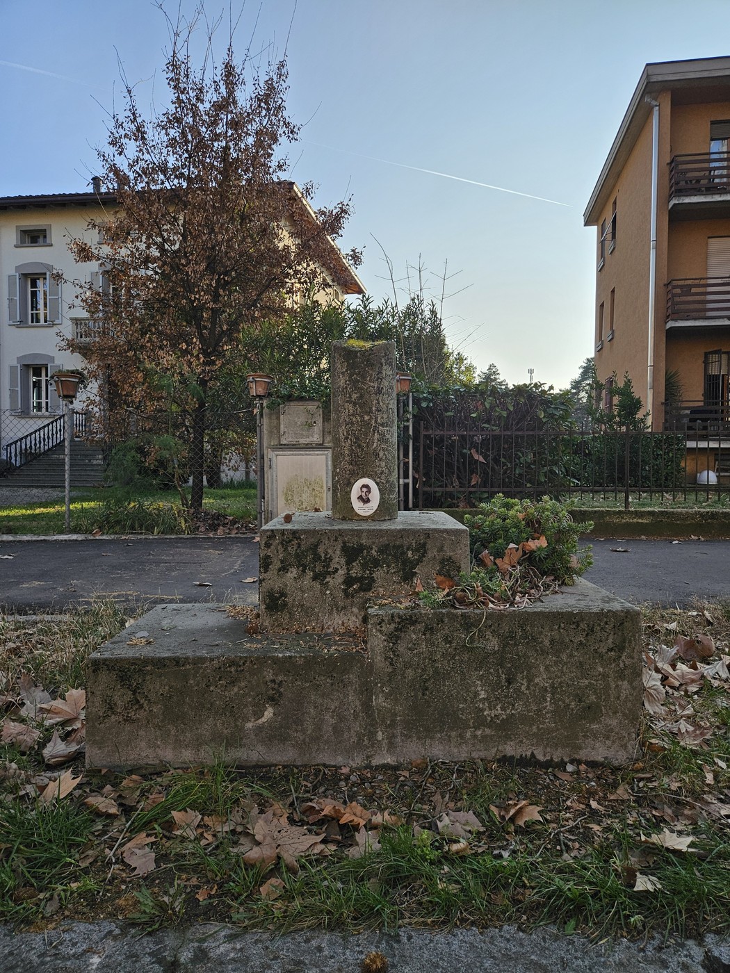 Cippo in muratura con decorazioni vegetali, situato in un'area residenziale tranquilla.