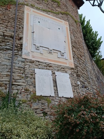 Monumento ai caduti in pietra, con liste scolpite e un design semplice, circondato da vegetazione.