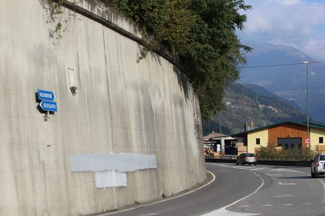 Lapide commemorativa dedicata a Donda e Pezzoli, situata lungo una strada in un contesto montano.