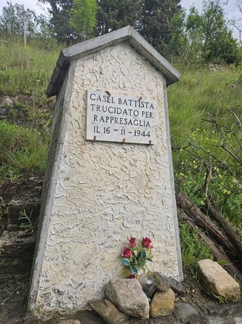 Cippo commemorativo a Casel, dedicato a una vittima di rappresaglia, con fiori e vegetazione circostante.