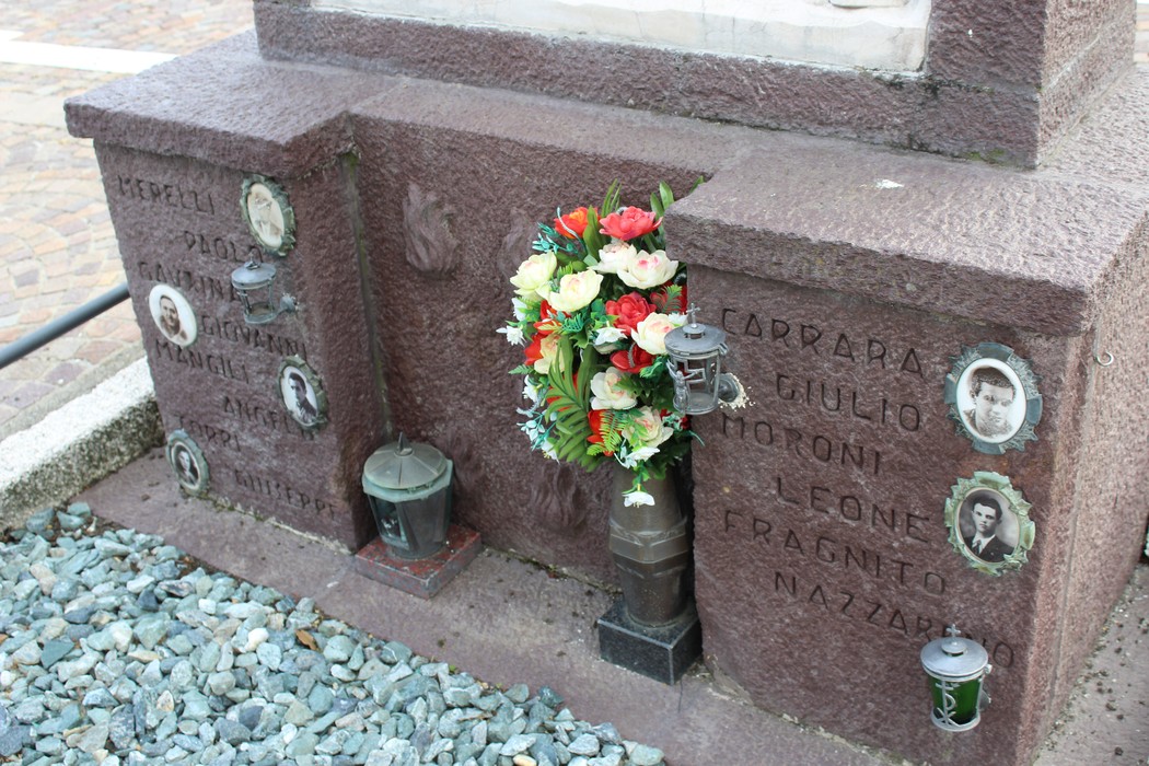 Monumento ai Caduti partigiani con fiori e lampade, dedicato alla memoria dei combattenti.