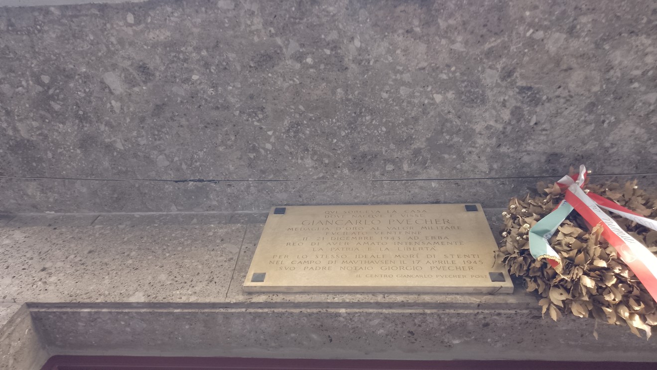Lapide commemorativa dedicata ai Puecher, con decorazione floreale e simboli patriottici.