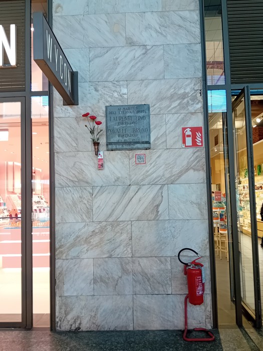 Lapide commemorativa dedicata a Laurenti e Davalle, situata su una parete di un locale commerciale.