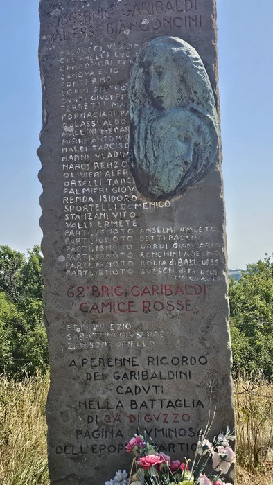 Stele commemorativa dedicata alla "62ª Brigata Garibaldi", situata a Ca' di Guzzo, circondata da fiori.