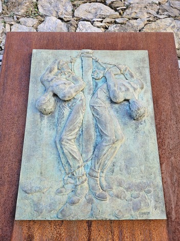 Scultura che rappresenta due figure umane in un atto di unione e tensione, collocata in un contesto di pietra.