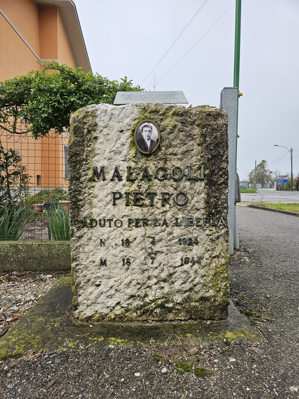Cippo commemorativo in pietra dedicato a Pietro Malagoli, situato lungo una strada.