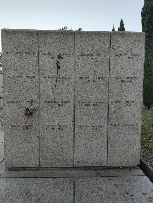 Monumento commemorativo con lastre di pietra, dedicato ai caduti, ornato da tributi floreali e messaggi di ricordo.