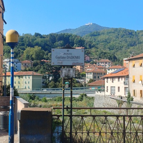 Cartello stradale intitolato al ponte, con iscrizione, su un ponte cittadino tra i monti.