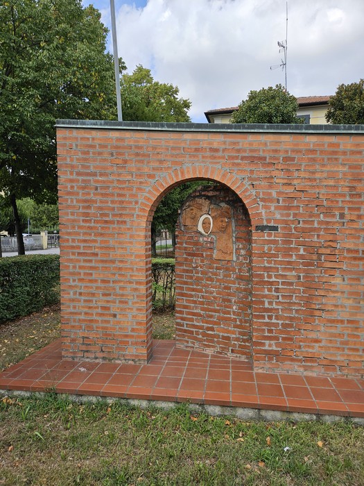 Monumento alla Resistenza con struttura in mattoni e arco, immerso nel verde di un parco.