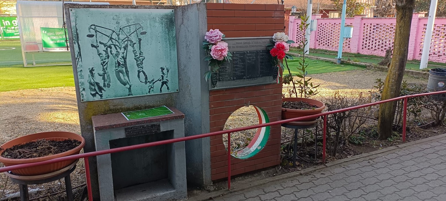 Monumento ai caduti con sculture commemorative e fiori decorativi, situato in un’area verde.