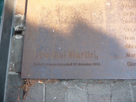Stele commemorativa per i Tredici Martiri, con iscrizioni su superficie metallica, situata all'aperto.