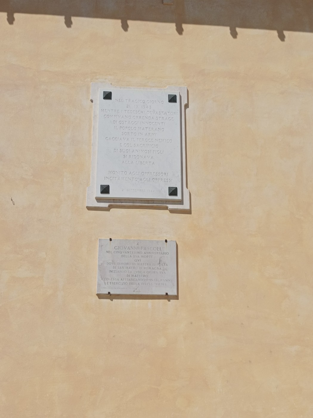 Lapide commemorativa dedicata alla liberazione di Matera, affissa su un muro giallo.