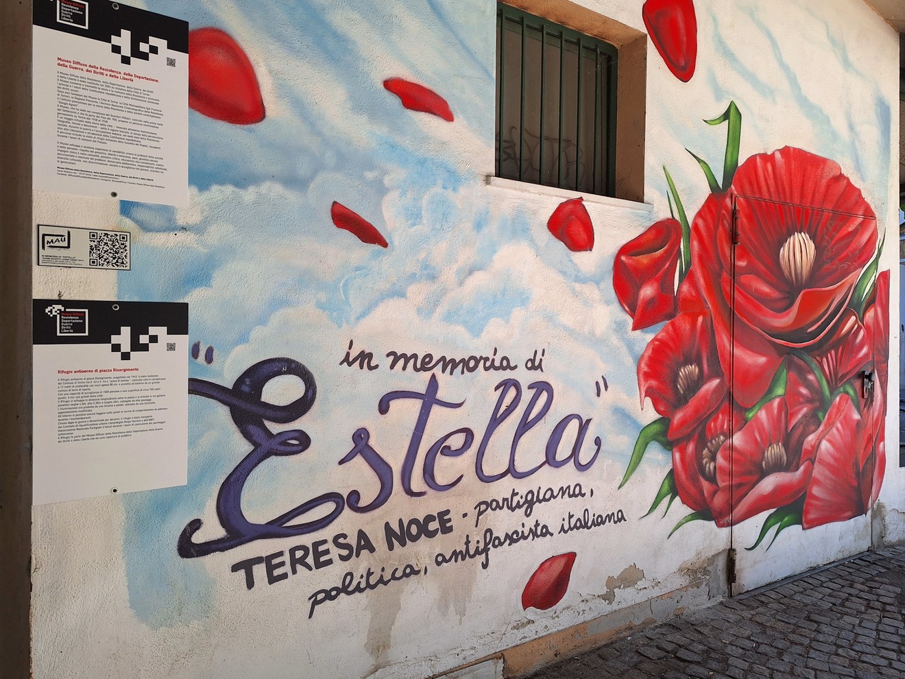 Murale commemorativo di Estella, con rose rosse su sfondo azzurro e testo in memoria della partigiana Teresa Noce.