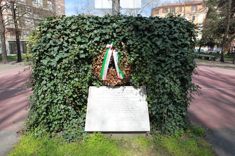 Lapide commemorativa immersa nel verde, con una corona di fiori tricolore, in memoria della battaglia della Bolognina.