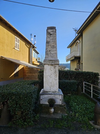 Monumento ai Caduti di Limone, obelisco in marmo circondato da vegetazione e edifici storici.