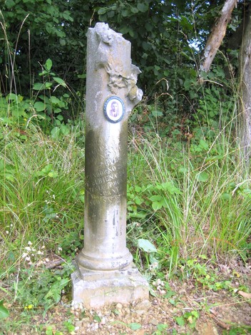 Cippo commemorativo a Bonino, immerso nella vegetazione, con dettagli floreali e una placca centrale.
