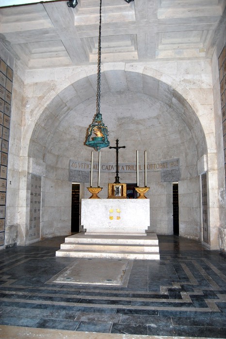 Interno del "Sacrario dei caduti militari a Trilj" con altarino, croce e decorazioni, ambiente sobrio e commemorativo.