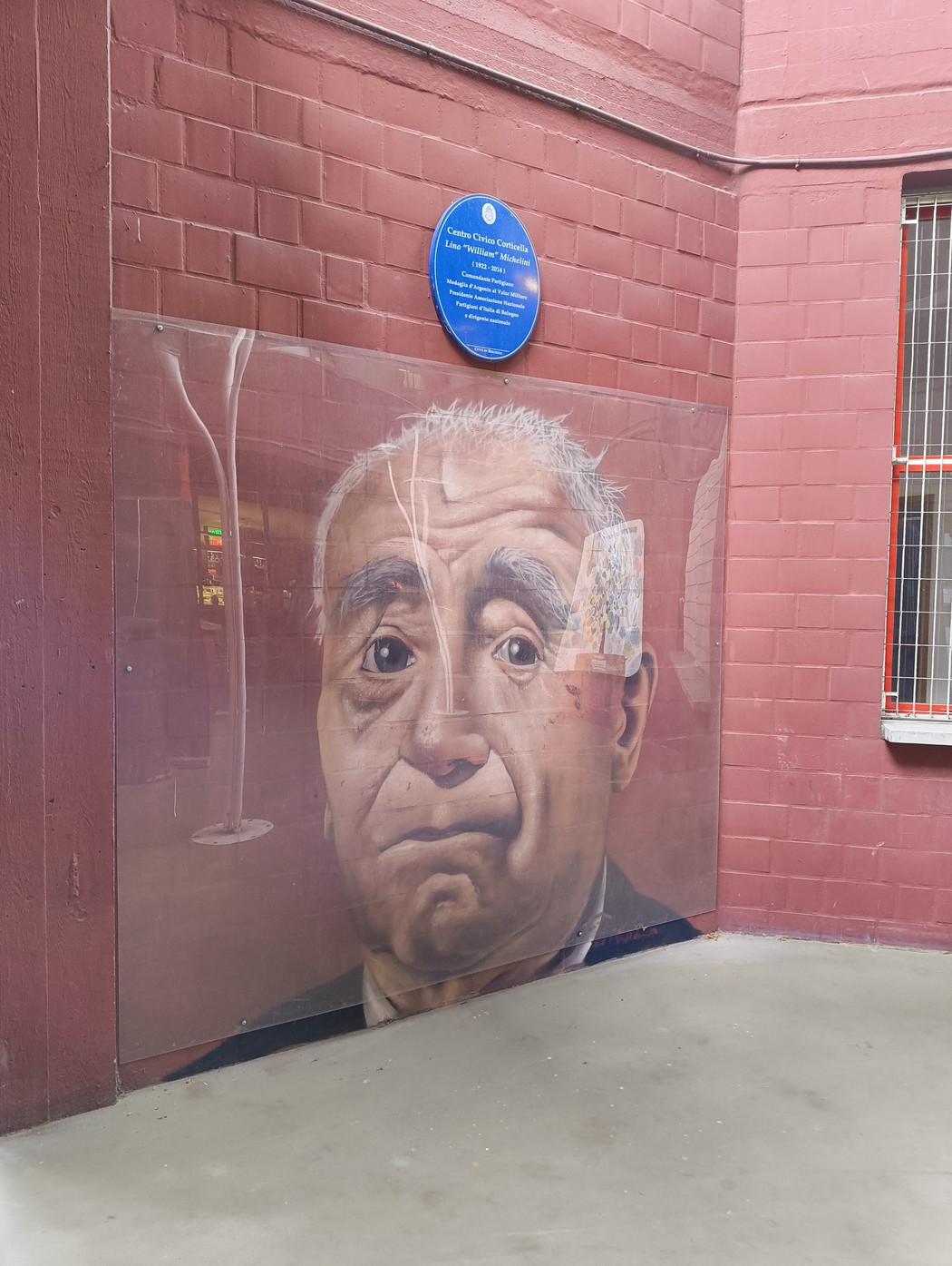 Murale che ritrae un anziano con espressione pensierosa, collocato in una cornice urbana caratterizzata da mattoni rossi.