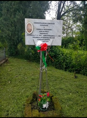 Targa commemorativa dedicata a Giovannini, circondata da vegetazione e decorazioni floreali.