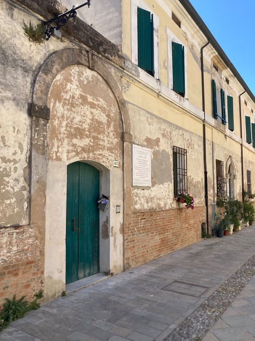Lapide a Goia su un muro di un edificio storico con porte verdi e dettagli architettonici in un contesto urbano.