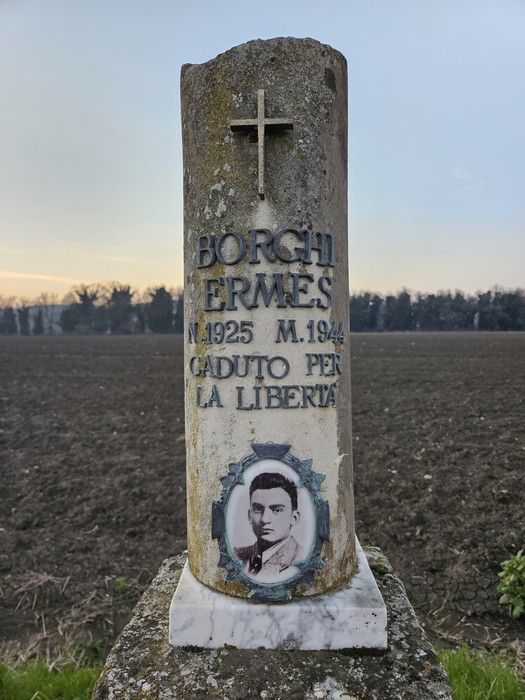 Cippo commemorativo dedicato a Ermés Borghi, caduto per la libertà, con un'immagine e una croce sopra.