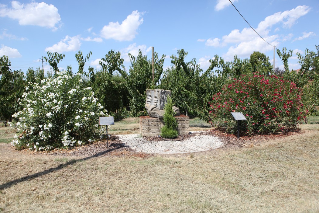 Monumento ai Caduti della Libertà circondato da piante fiorite e verde, in un ambiente sereno e naturale.