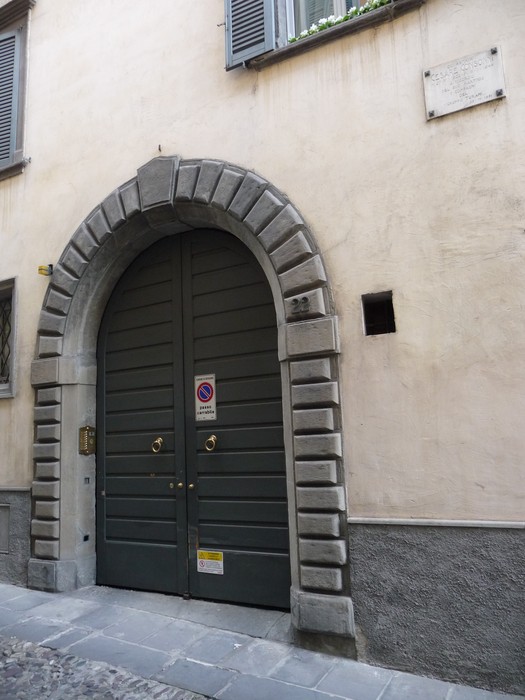 Ingresso di un edificio storico con una grande porta verde e una lapide murale affissa sopra.