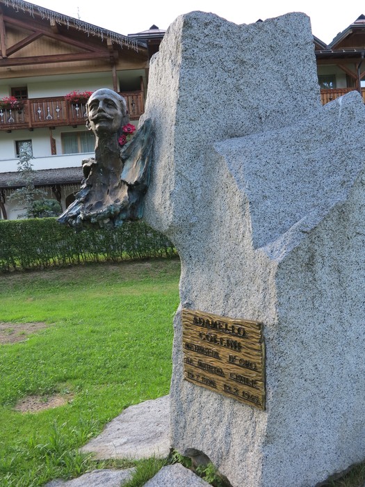 Monumento a Collini, scultura in bronzo su base di pietra, immerso nel verde. Rappresenta un omaggio significativo.