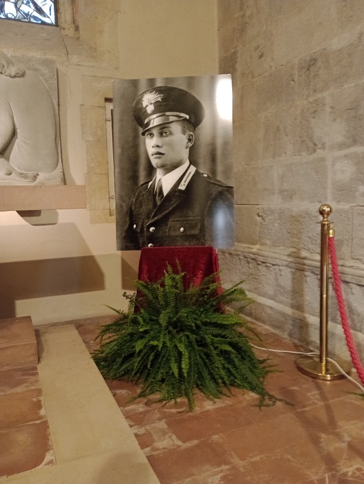 Il sepolcro di D'Acquisto, con un ritratto di lui in uniforme e decorazioni floreali.