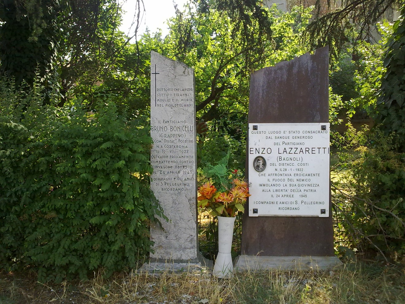 Lapide commemorativa di Lazzaretti con decorazioni floreali, situata in un contesto naturale.