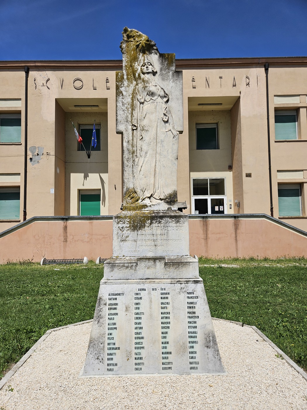 Monumento ai Caduti con statua e liste commemorative, situato davanti a un edificio scolastico.