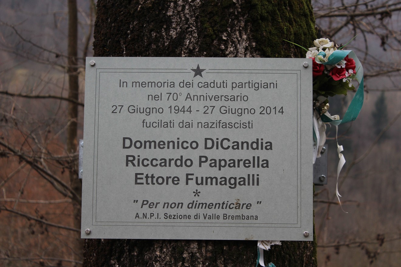 Targa commemorativa in memoria dei caduti partigiani con nomi e decorazioni floreali.