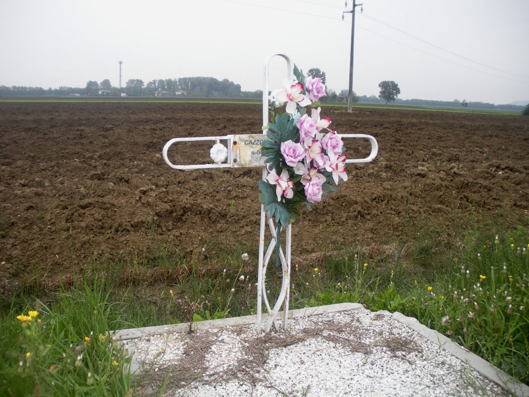 Croce a Cazzola con fiori artificiali, situata in un campo nella campagna italiana.