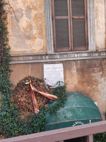 Lapide commemorativa a Perpetua, decorata con foglie e nastro, in un contesto storico.