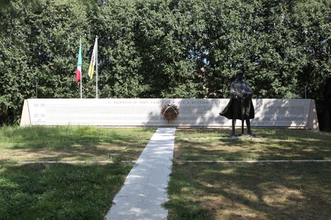 Monumento ai Caduti con una statua e una lastra commemorativa circondata da alberi.