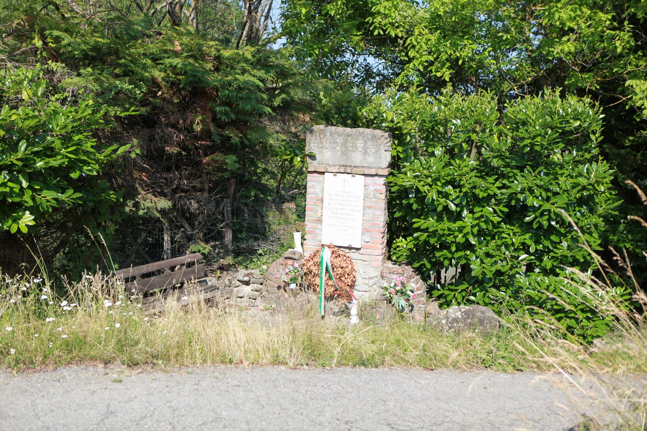 Monumento ai partigiani di Ca' di Bue, circondato da vegetazione e con una panchina vicina.