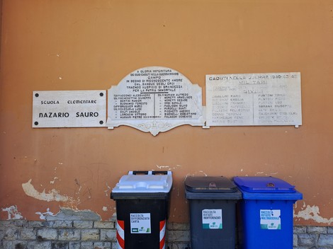 Lapidi commemorative dedicate ai caduti, con rifiuti in evidenza sul marciapiede.