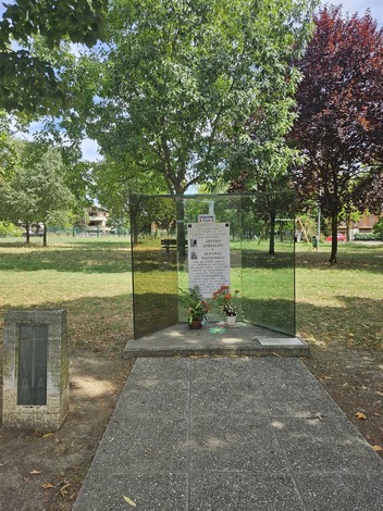 Monumento ad Anderlini e Paltrinieri, circondato da alberi e verde, con una struttura trasparente e fiori.